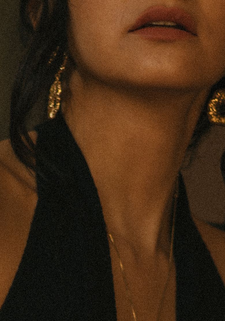 Woman wearing gold hoop earrings and a delicate gold necklace, dressed in a black halter top.