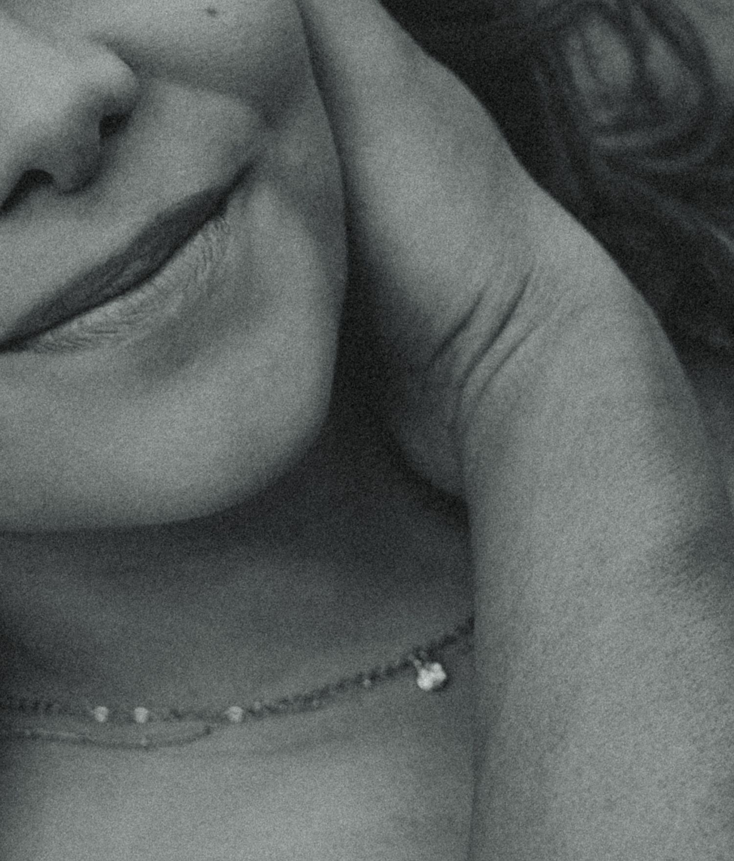 Black and white close-up portrait of a woman wearing a delicate chain necklace, resting her hand near her face.