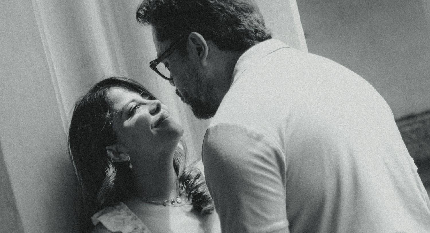 Black and white photo of a couple sharing an intimate moment, smiling and leaning close together.