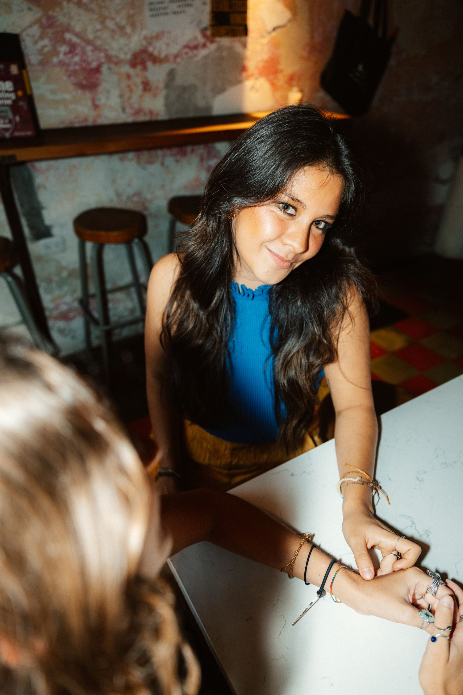Young woman in blue top smiling at camera while sitting at white table in restaurant.