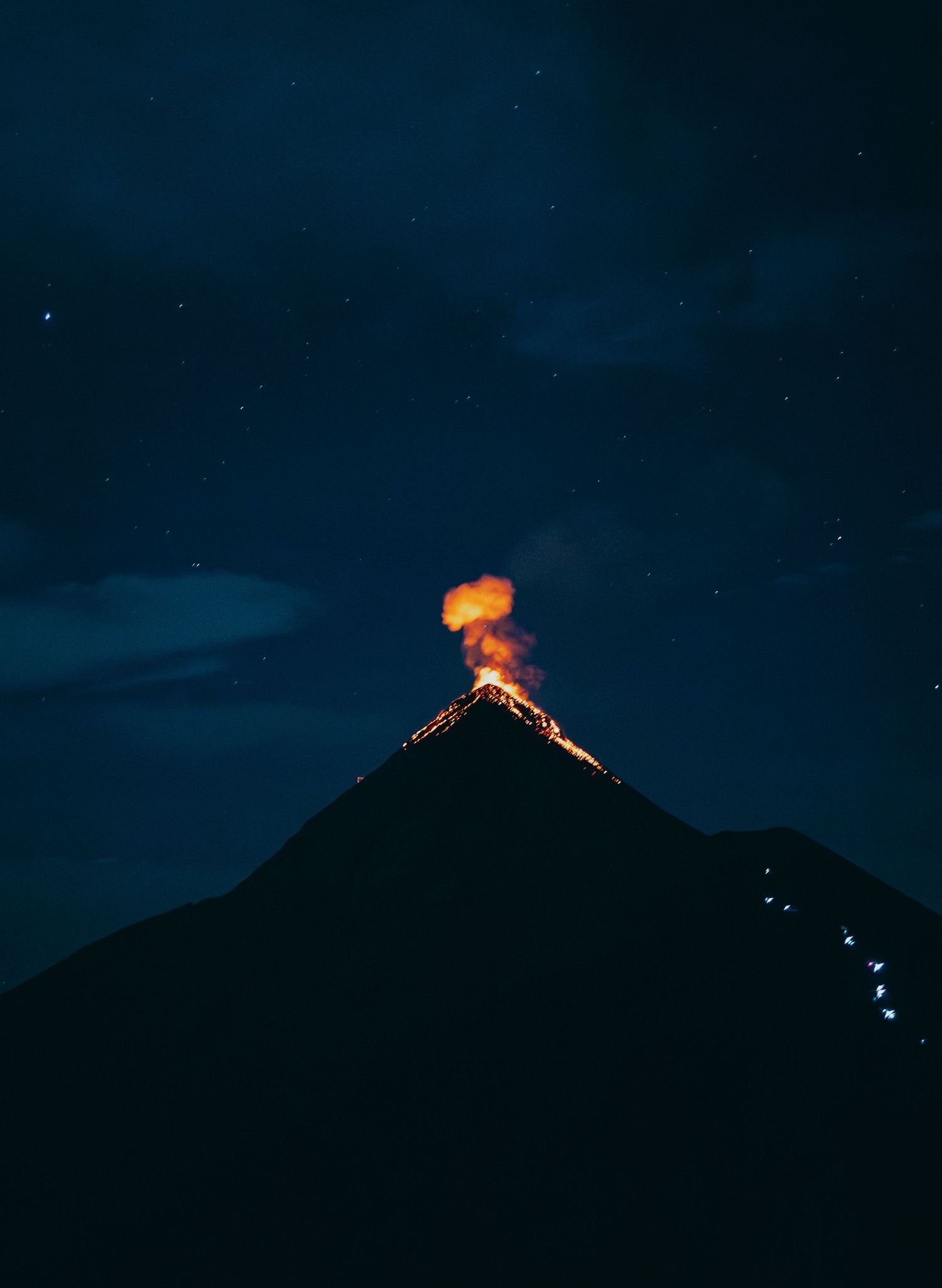 A volcano erupting with glowing lava and orange smoke against a dark starry night sky.