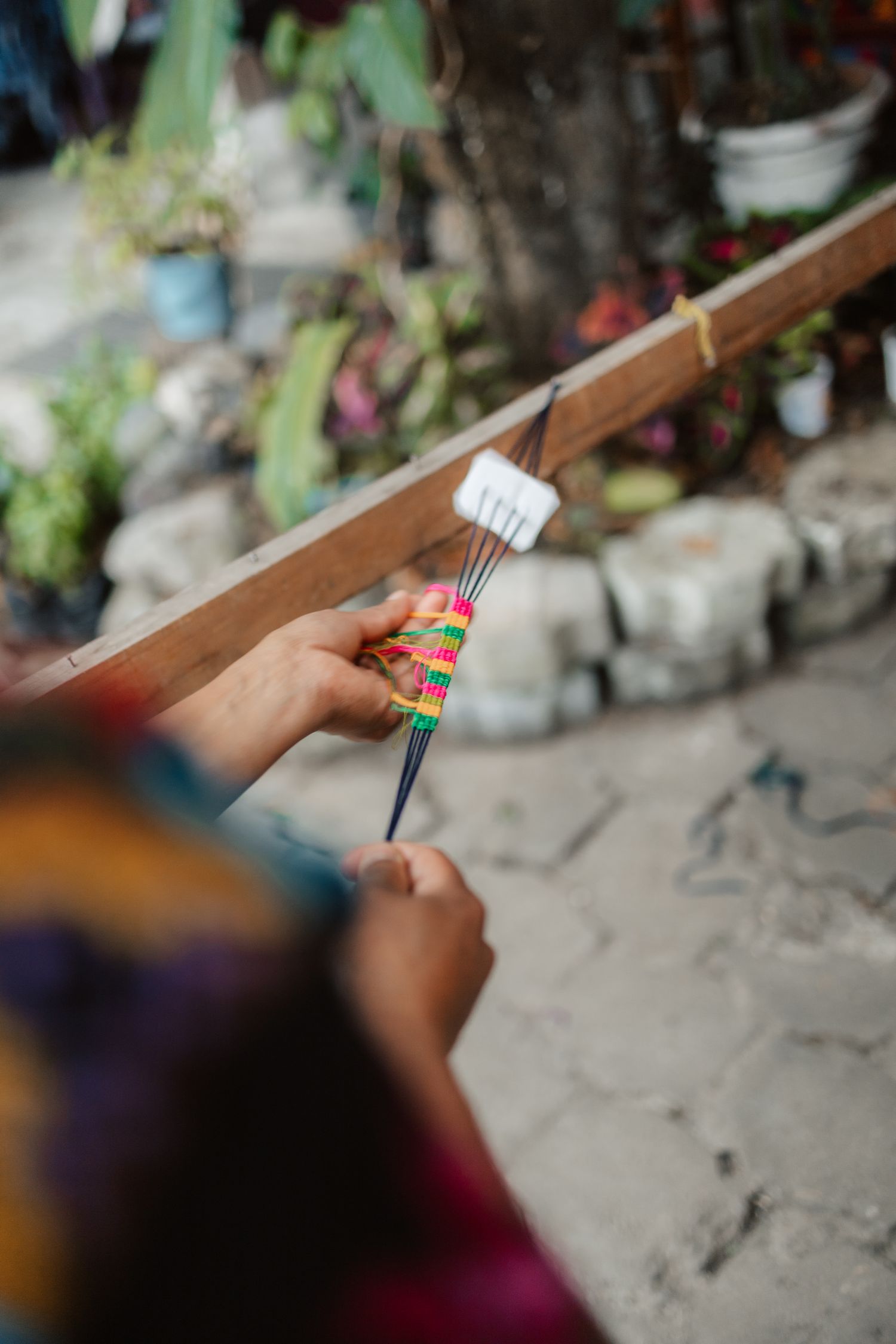 Close-up of hands weaving colorful threads on a loom in a traditional textile craft setting outdoors.