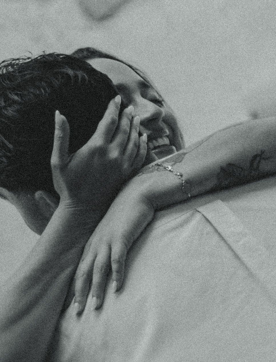 Black and white photo of two people in a warm embrace, one smiling with a hand cradling the other's head and a bracelet on the wrist.