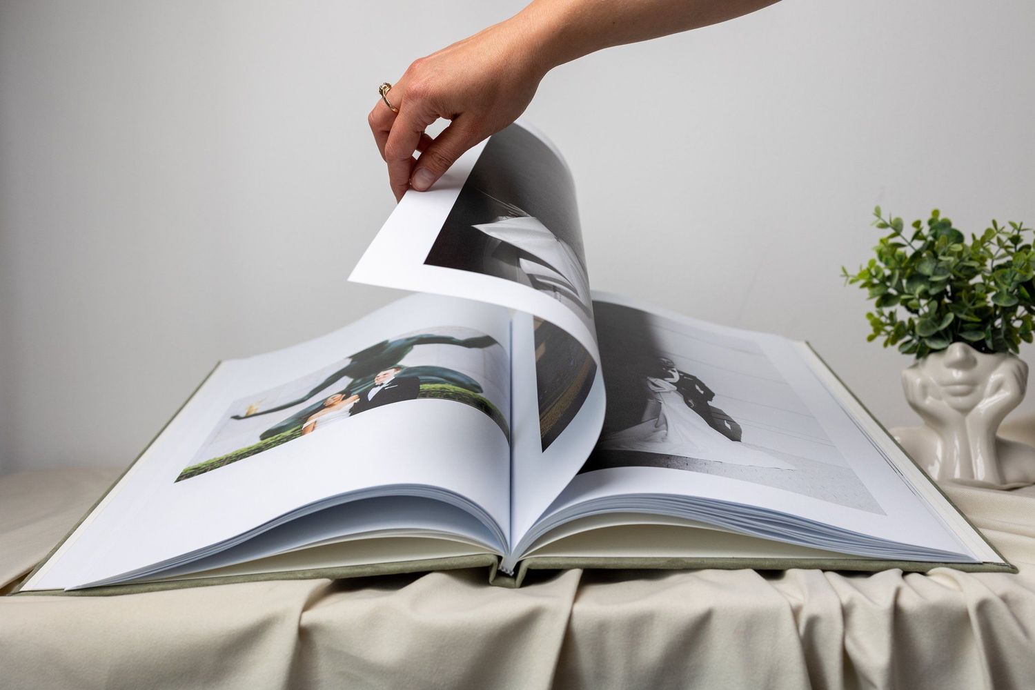 Hand turning pages of an open photo book with large printed images on a draped table.