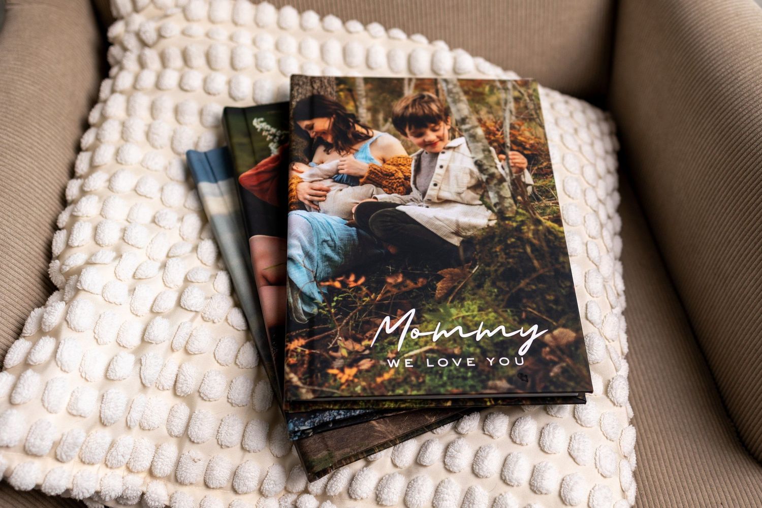 Stack of personalized photo books reading Mommy We Love You on a textured cream blanket.