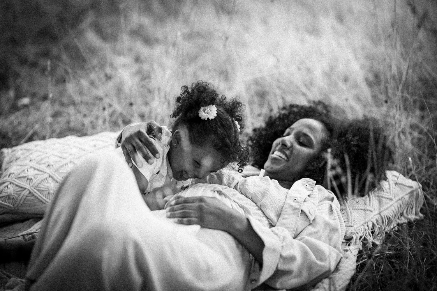 Black and white photo of a mother and daughter lying together laughing in tall grass.