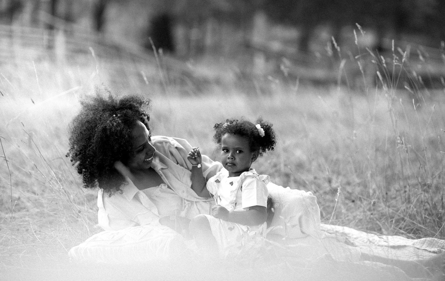 Black and white photo of a mother and young daughter sitting together in a grassy meadow.