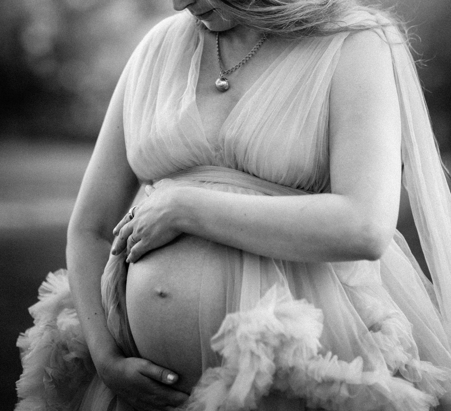 Black and white maternity photo of a pregnant woman in a flowing tulle gown.
