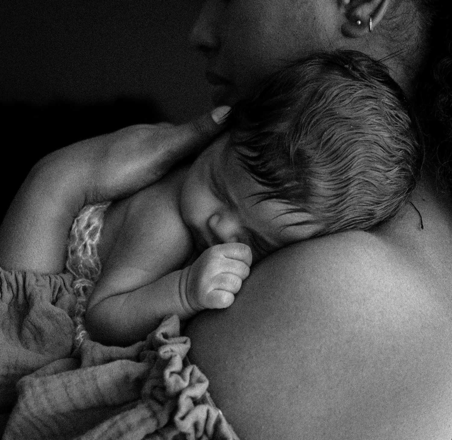 Black and white close-up of a newborn baby resting on a mothers shoulder.