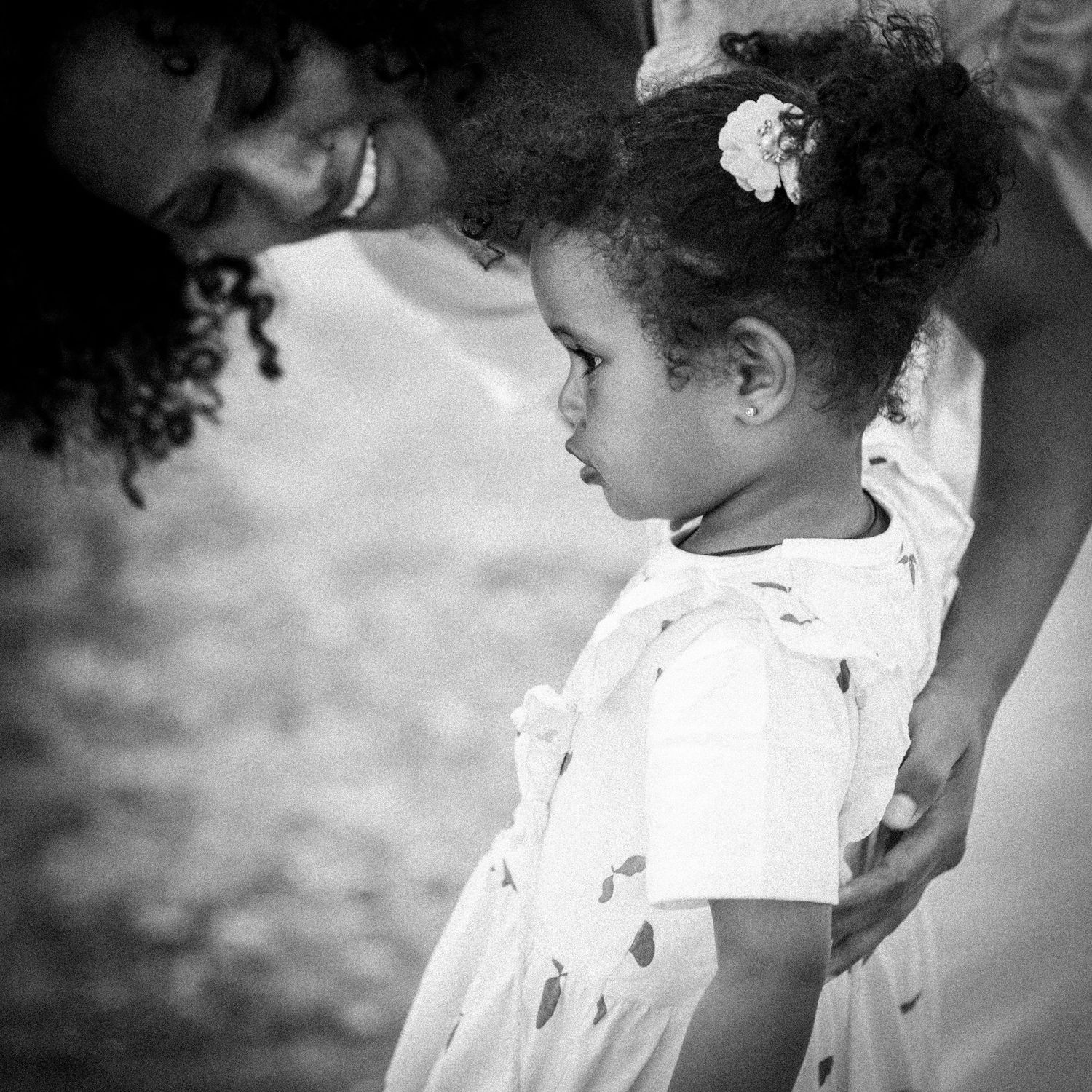 Black and white portrait of a young curly-haired girl with a flower clip standing with her mother.
