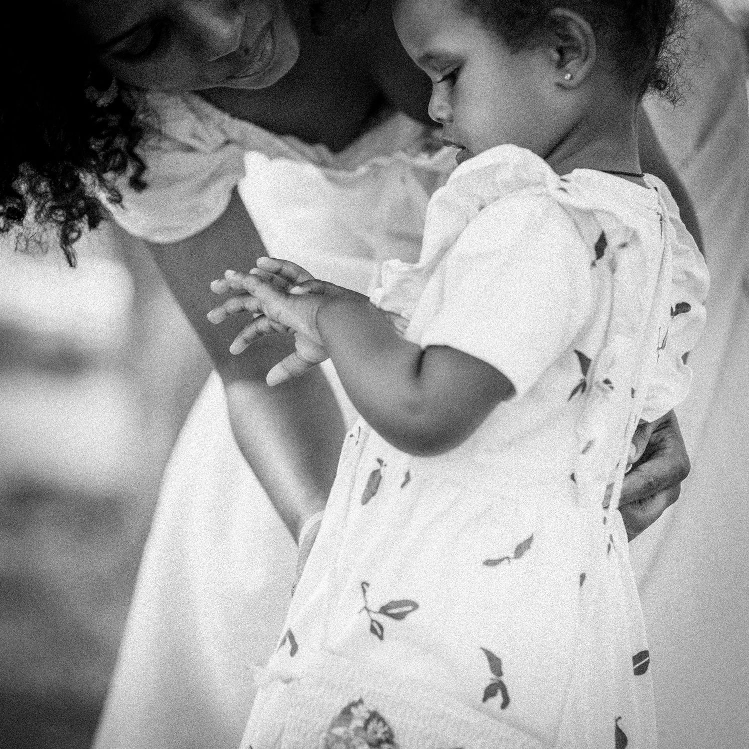 Black and white close-up of a mother holding her young child in a white dress.