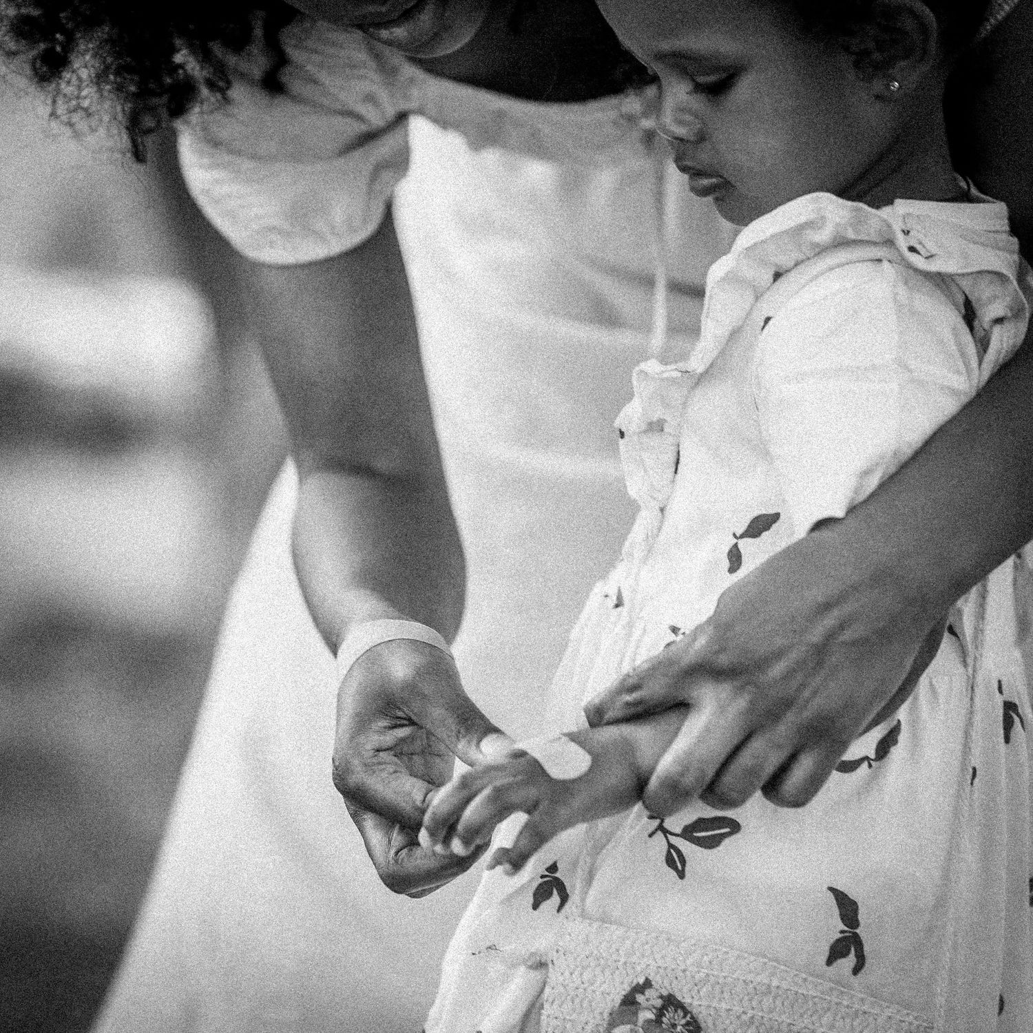 Black and white photo of a mother gently holding her toddler daughter's hands outdoors.
