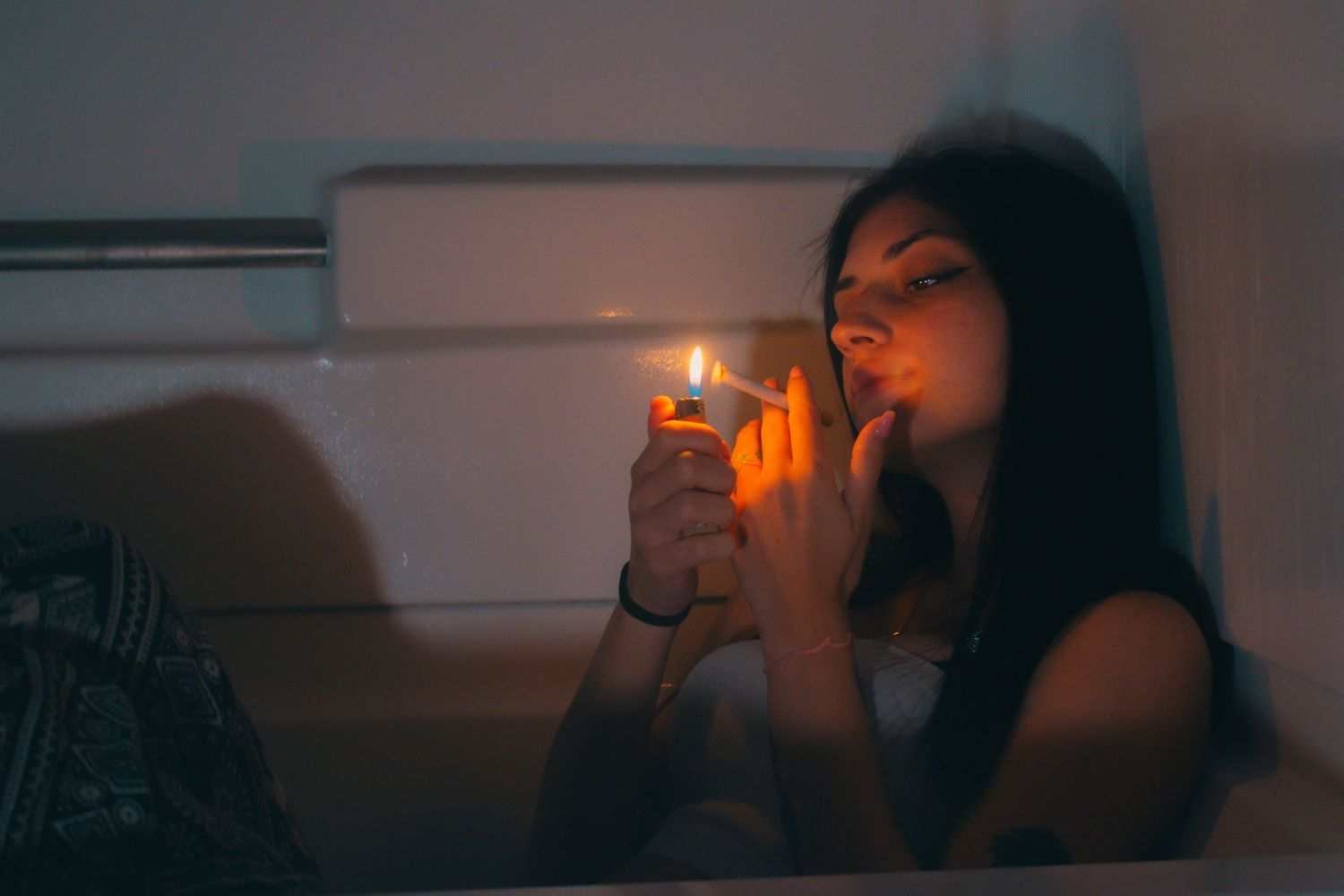 Young woman lighting a cigarette in a dark room with warm golden glow.