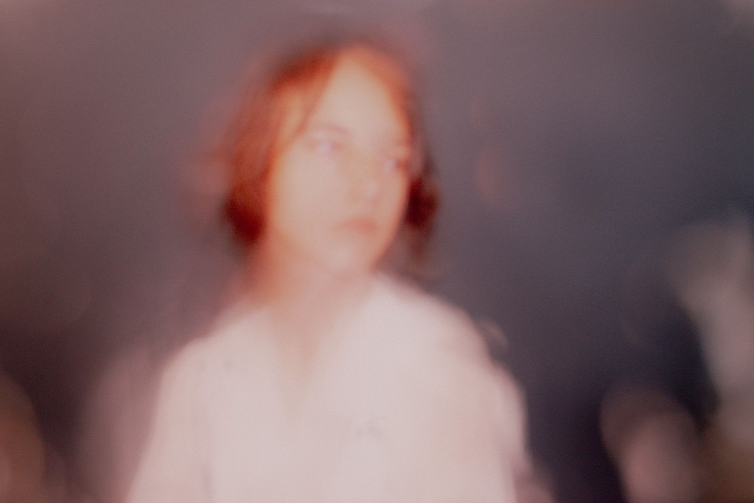 Blurry ethereal portrait of a person with red hair in soft dreamy light.