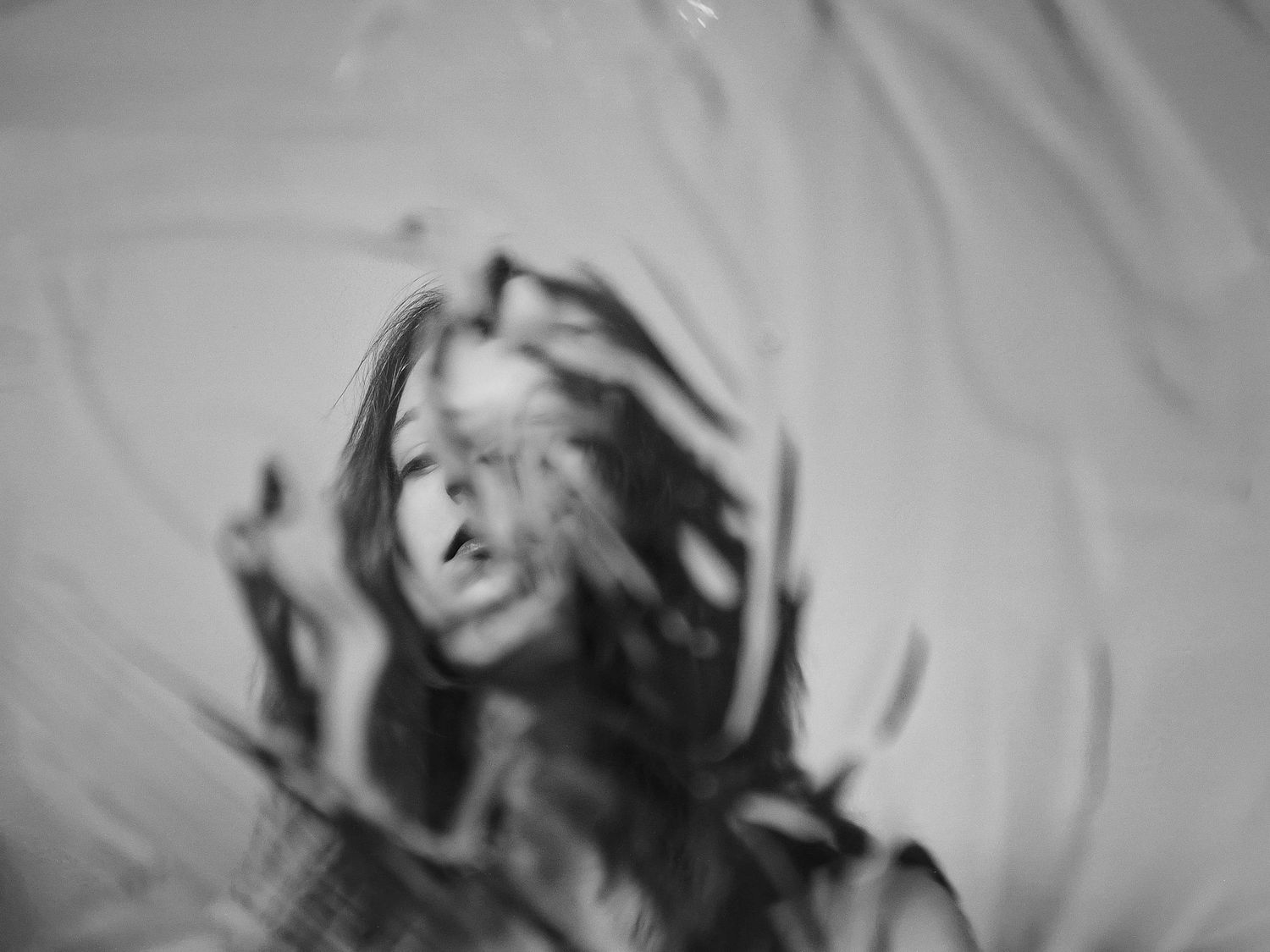 Artistic blurred black and white photo of a woman with wild hair pressed against glass.