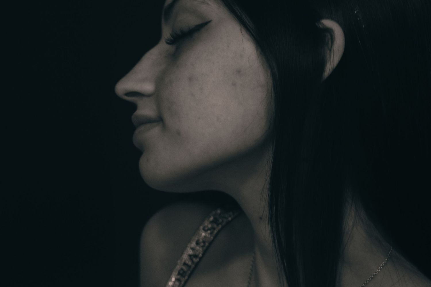 Black and white side profile portrait of a dark-haired woman with eyes closed on dark background.
