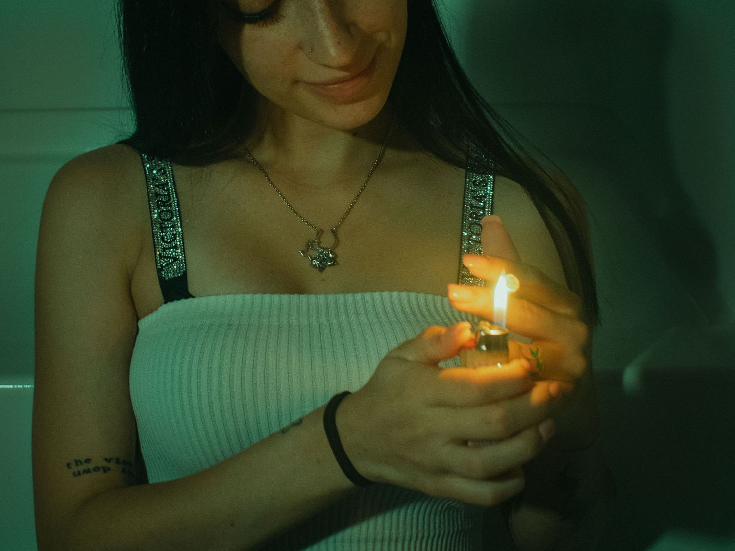 Smiling woman holding a lighter flame in a green-tinted dimly lit room.