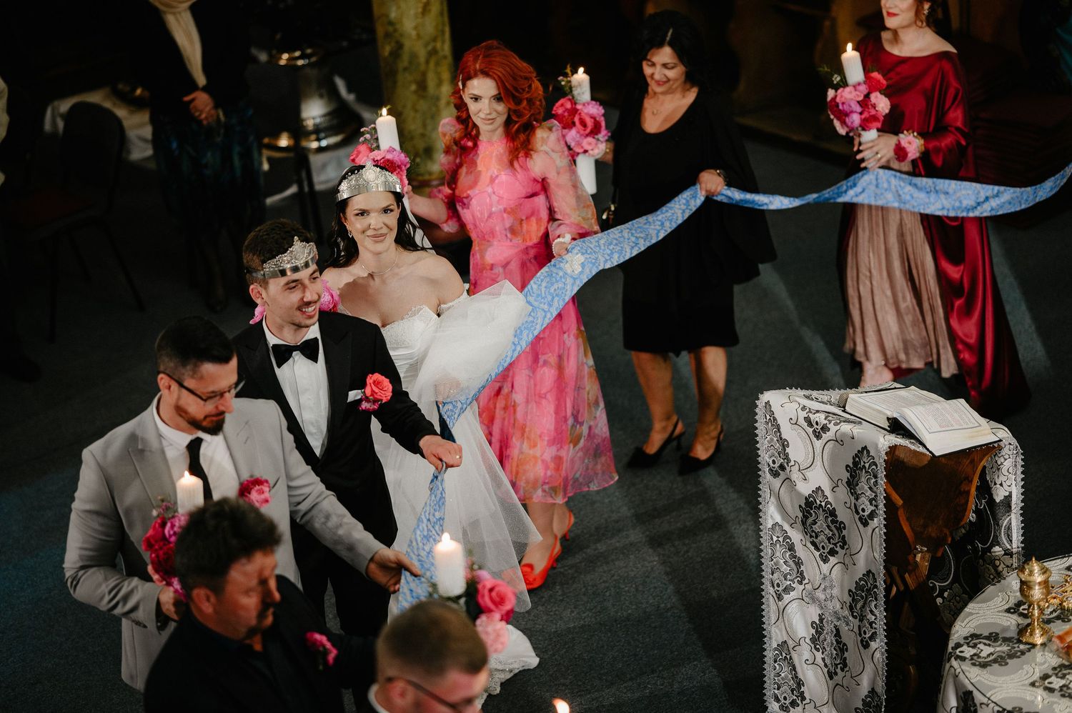 Bride and groom walk down the aisle with wedding party holding a blue ribbon in an ornate church.