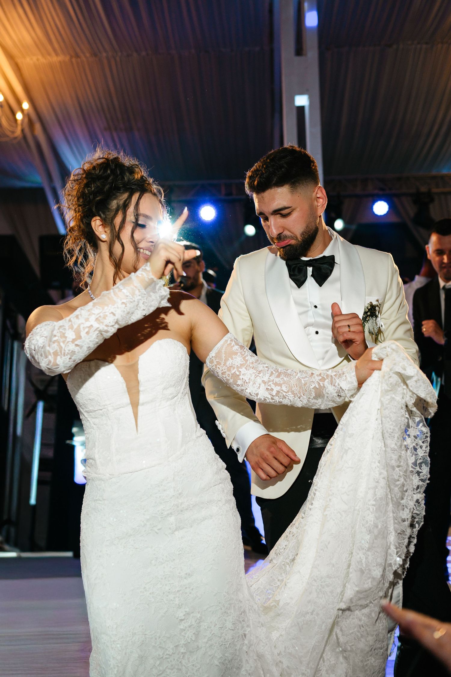 Bride and groom share their first dance, wearing elegant white wedding attire at a beautifully lit reception venue.
