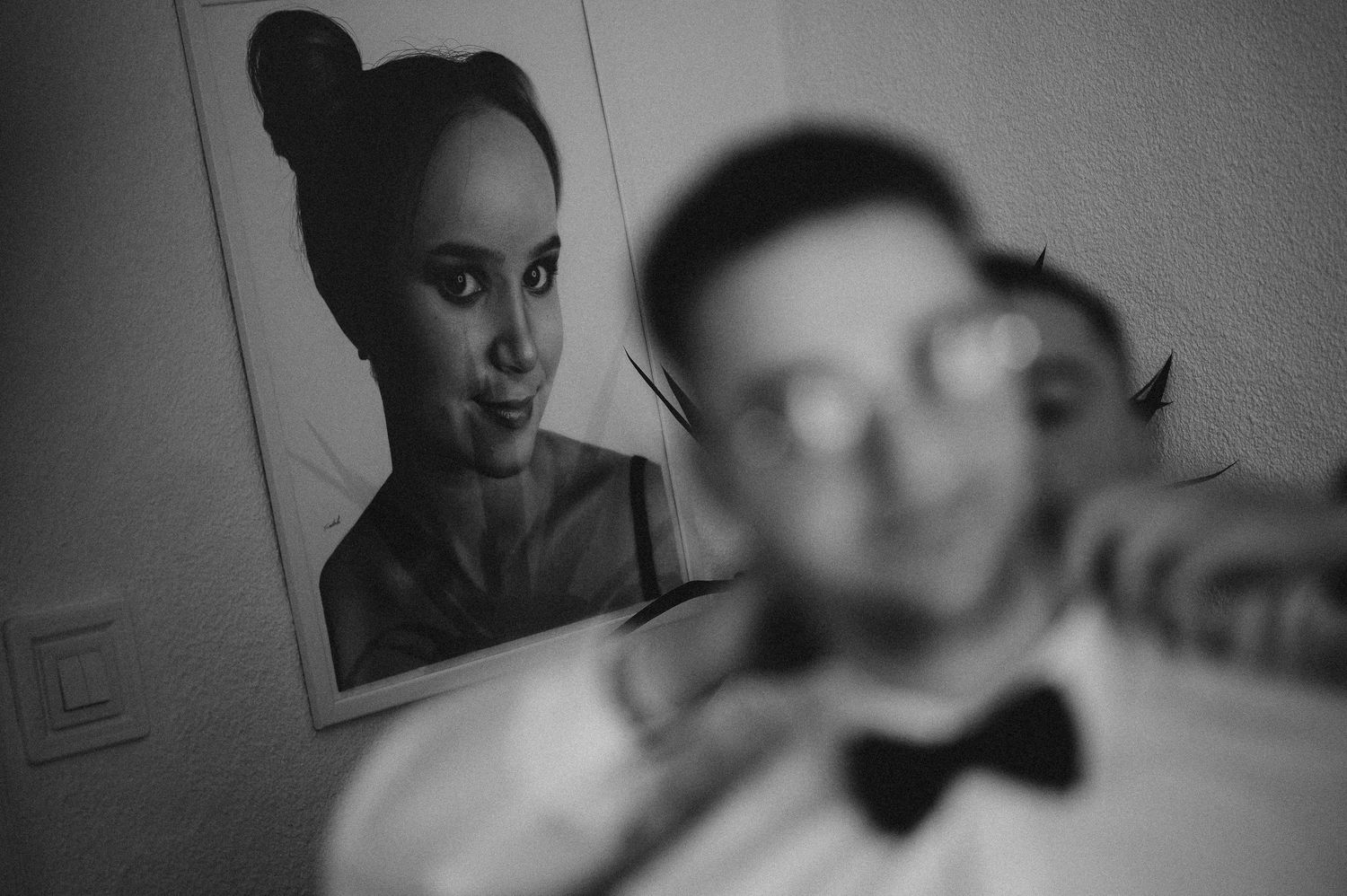 Black and white photo of a woman reflected in a mirror behind a blurred man wearing a bow tie.