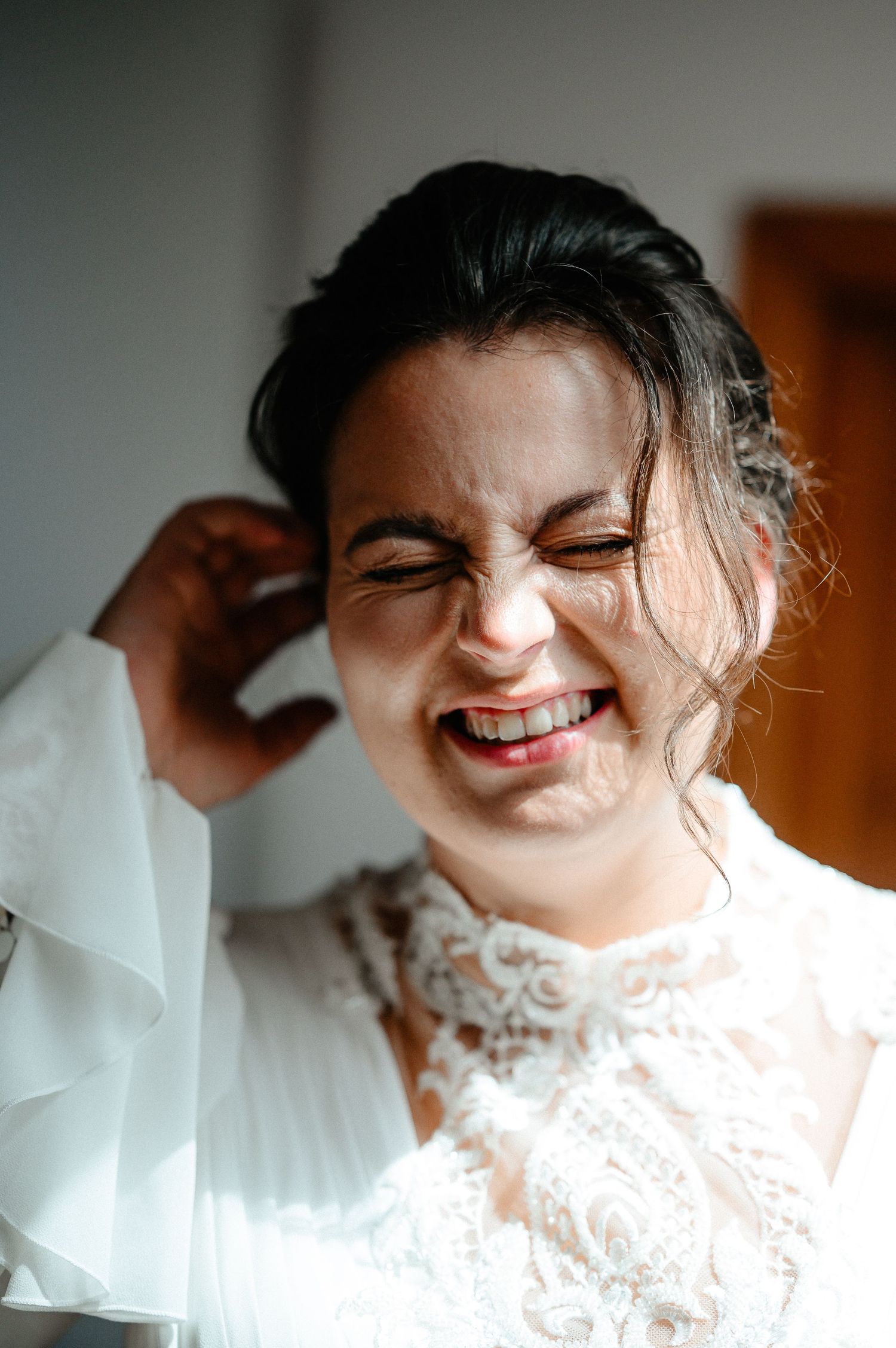 Bride laughing joyfully in lace wedding dress during bridal preparations.