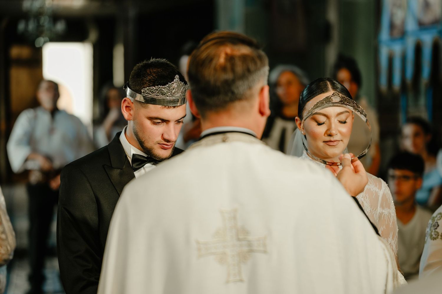 Groom and bride receive wedding crowns from Orthodox priest during traditional church ceremony.