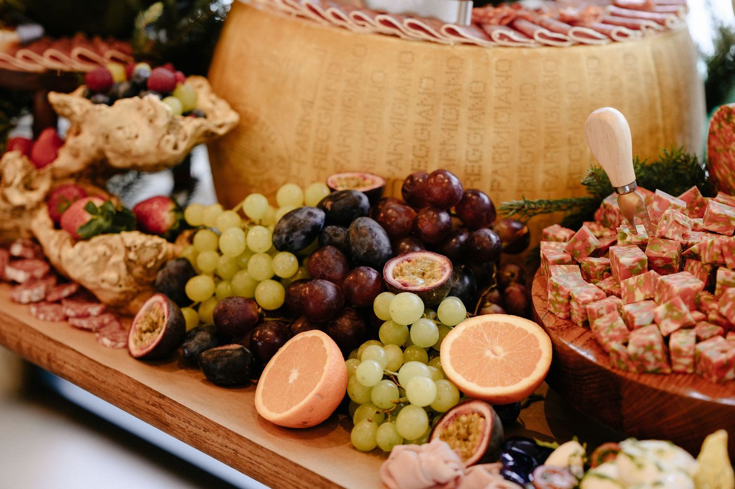 Gourmet charcuterie board featuring a large wheel of aged cheese, green grapes, figs, and cured meats.