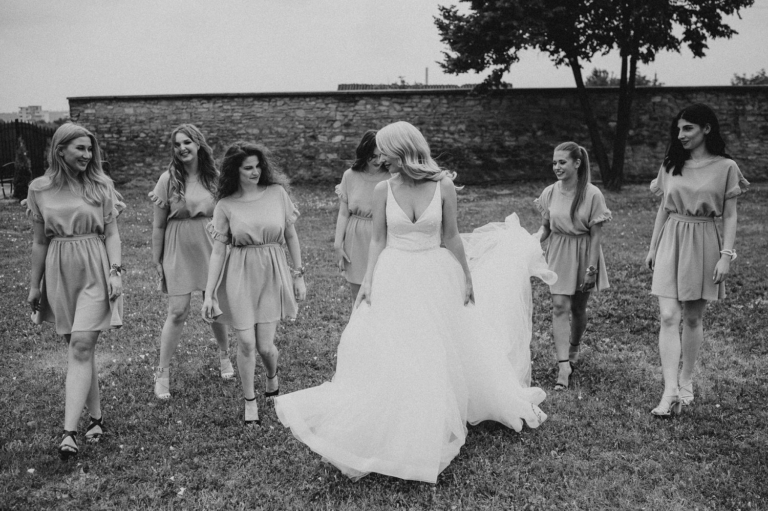 Black and white photo of bride and bridesmaids walking together on a grassy outdoor venue.