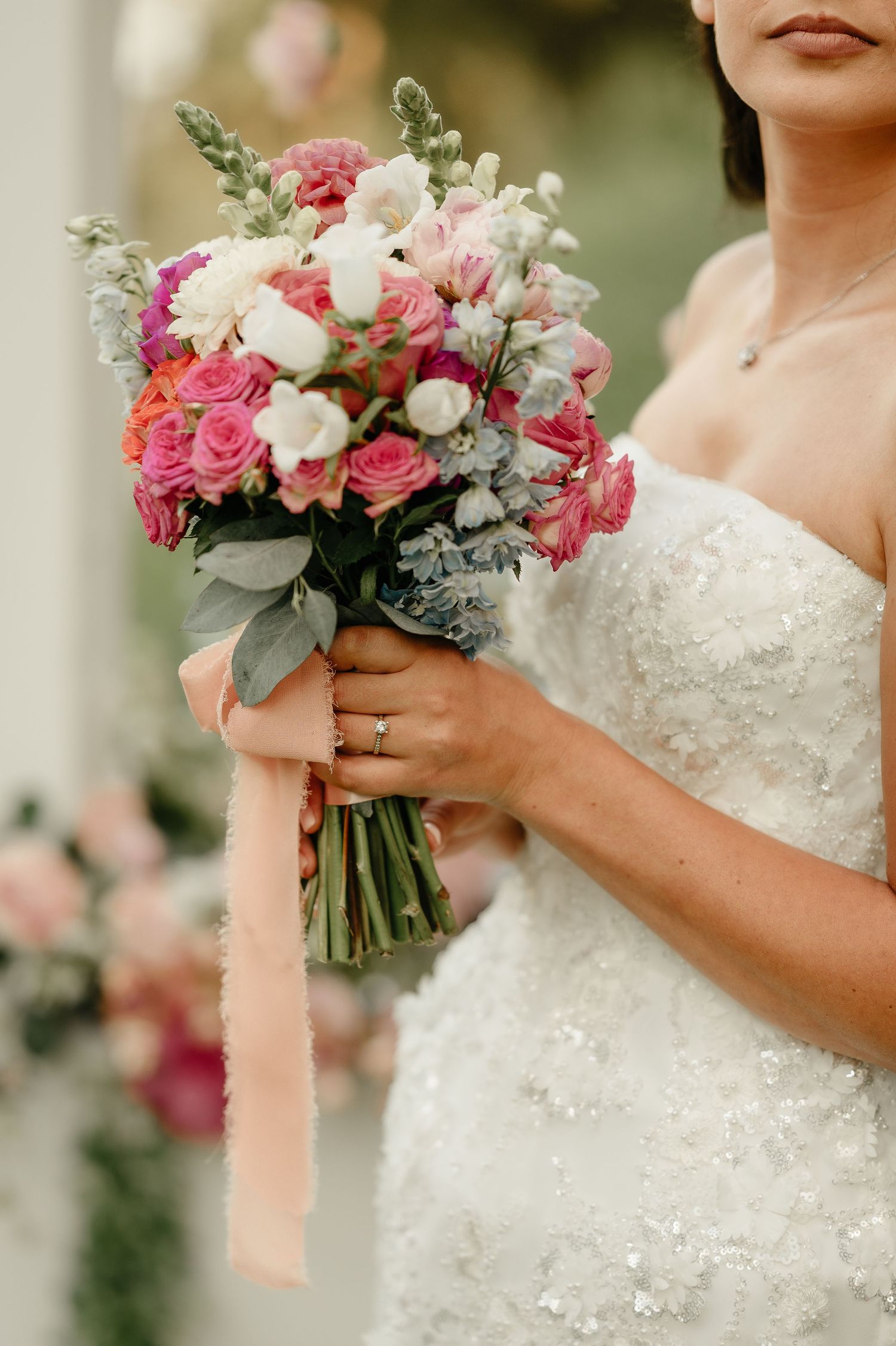 Bride holds a stunning pink and white rose wedding bouquet with peach ribbon detail.