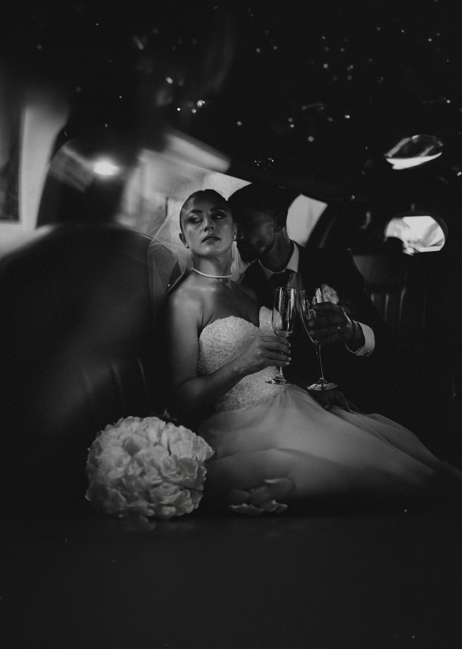 Black and white wedding photo of bride and groom in a limousine toasting with champagne glasses.