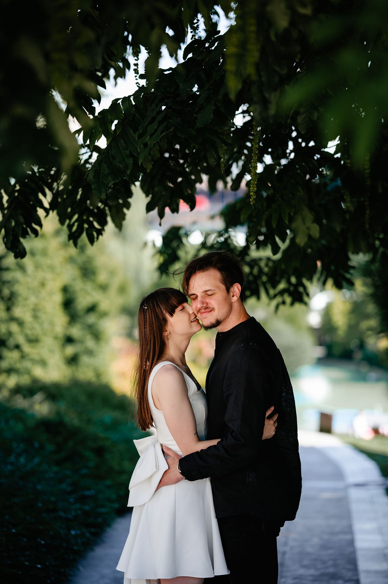 Happy couple hugging and smiling together beneath leafy tree branches in a park.