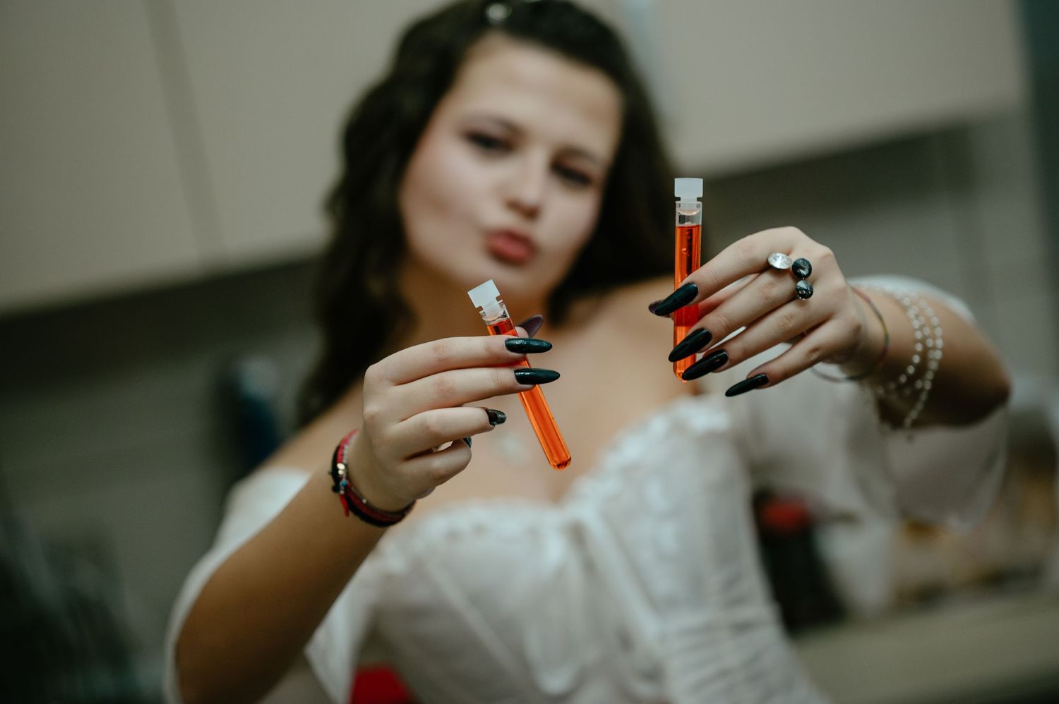 A woman with long dark nails holds two orange test tubes while wearing a white corset costume.