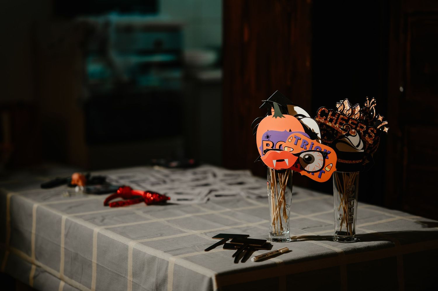 Halloween decorated table with orange pumpkin decorations in glass vases and scattered props in dim lighting.