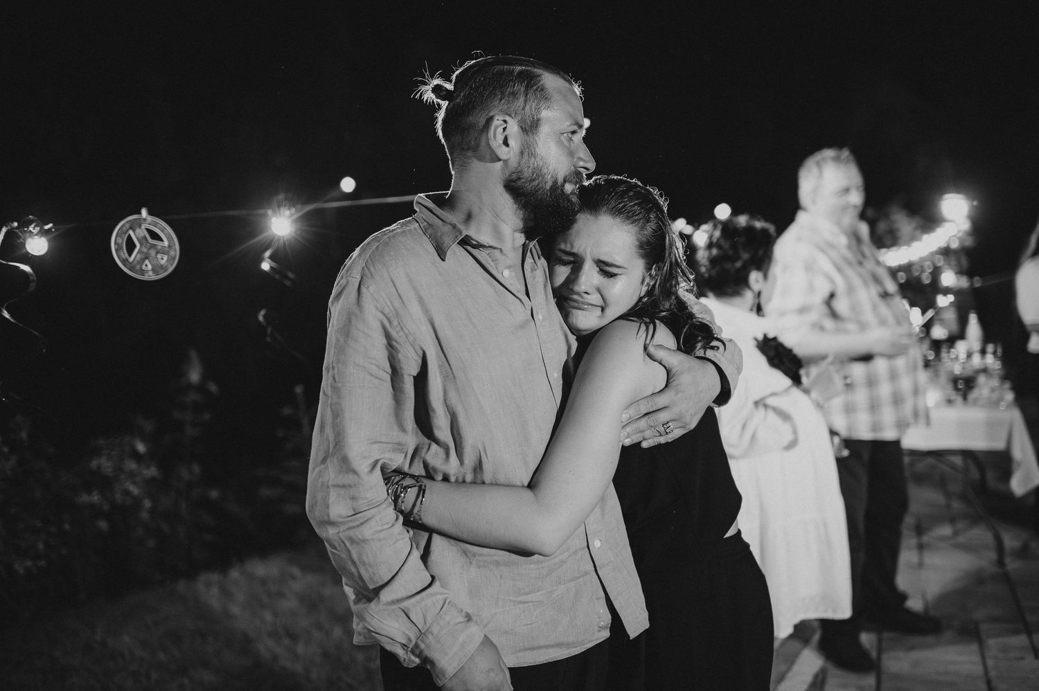 Black and white photo of a couple embracing warmly at an outdoor evening party.