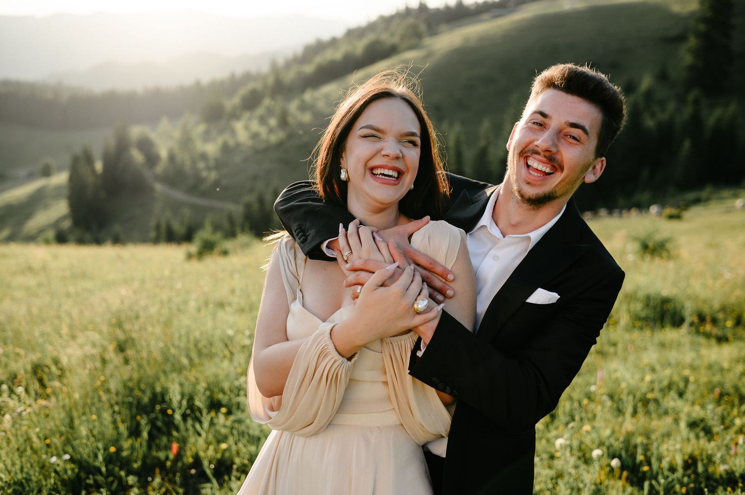 Laughing bride and groom embrace in a green mountain meadow during golden hour outdoor wedding photography.