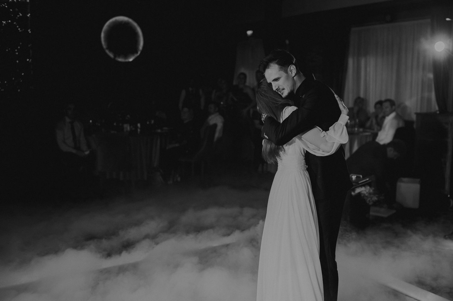 Bride and groom share romantic first dance surrounded by fog in black and white wedding photo.