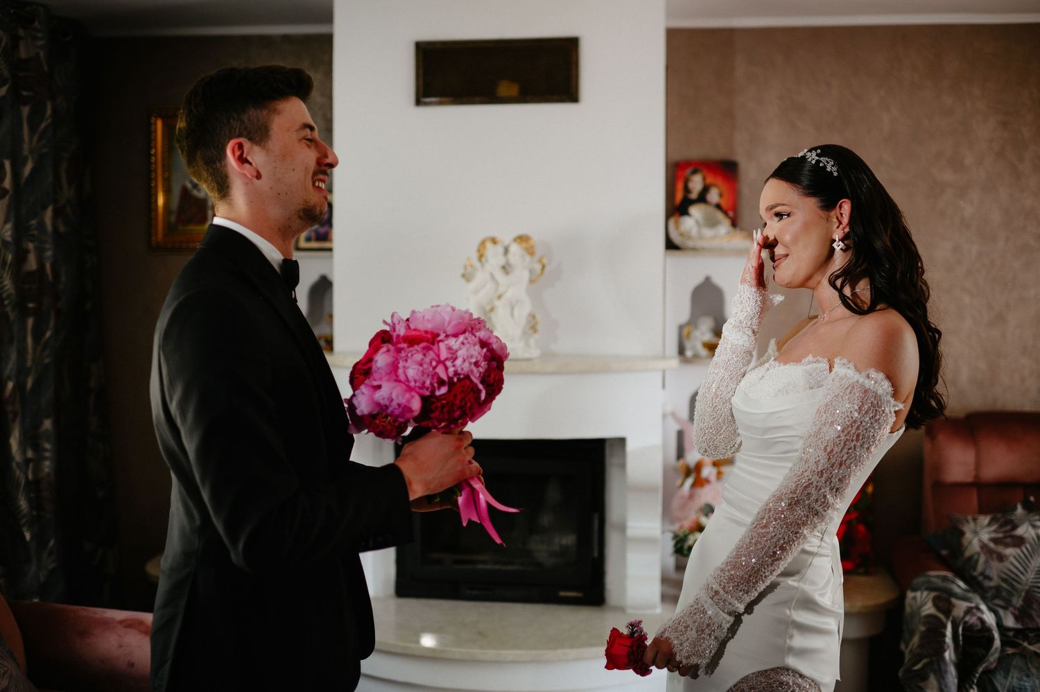 Emotional bride wipes tear during first look with groom holding pink peony wedding bouquet.