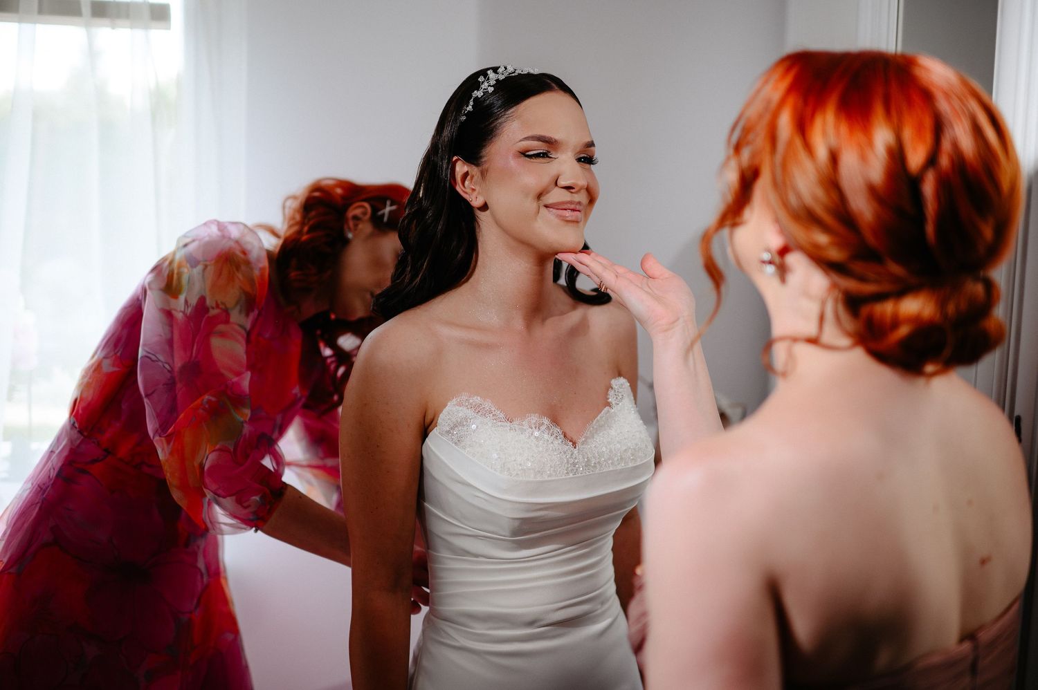 Bridesmaids helping smiling bride with final makeup touches before wedding ceremony.