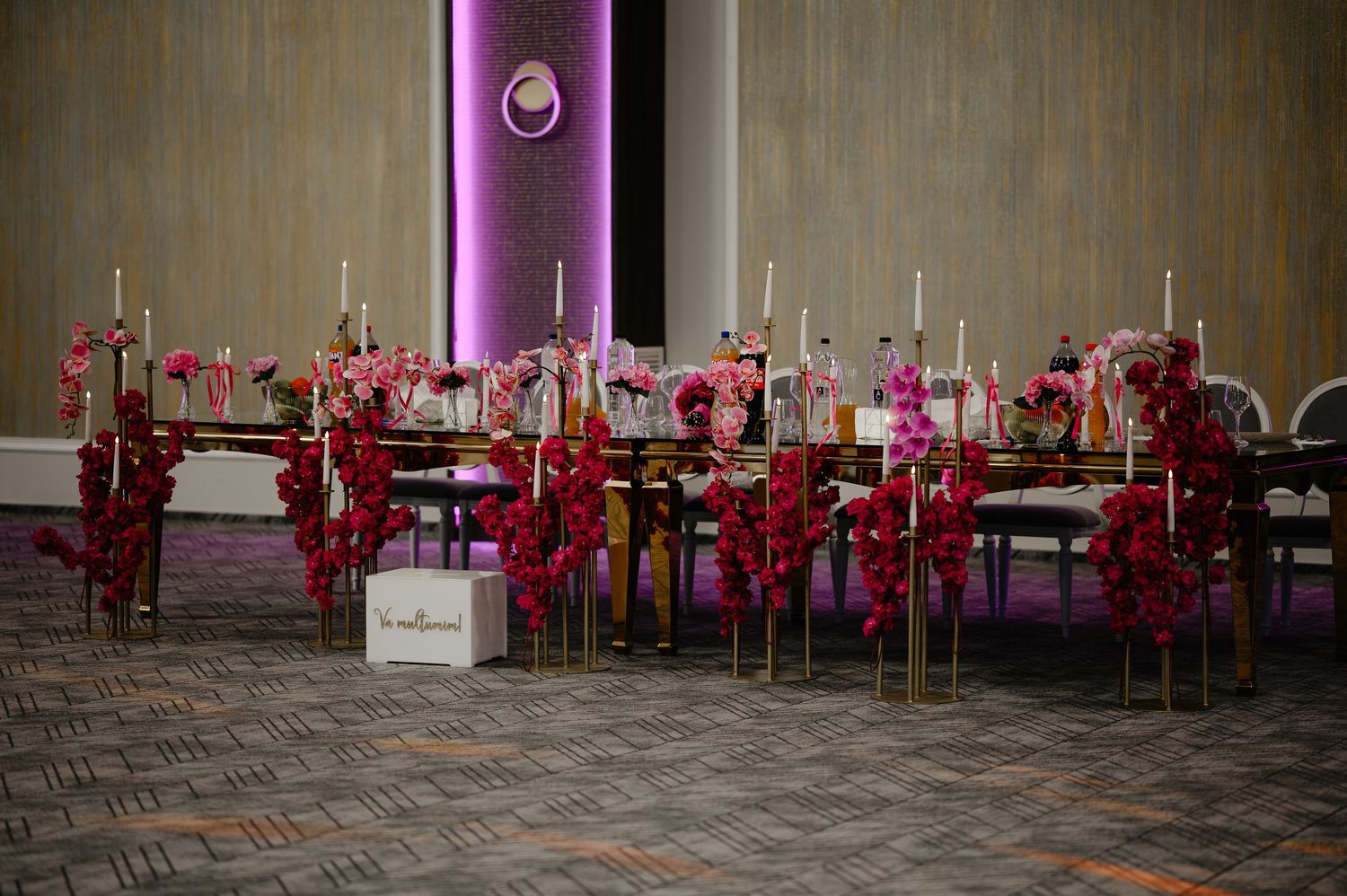 Wedding reception table with fuchsia floral garlands, gold candle stands, and gift box.
