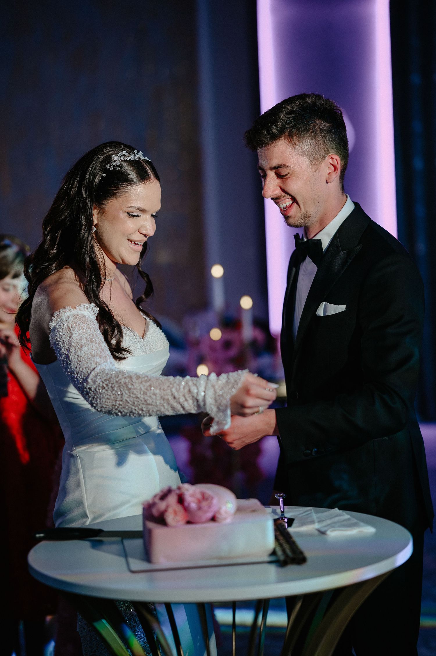 Laughing bride and groom cut their pink wedding cake together at elegant reception venue.