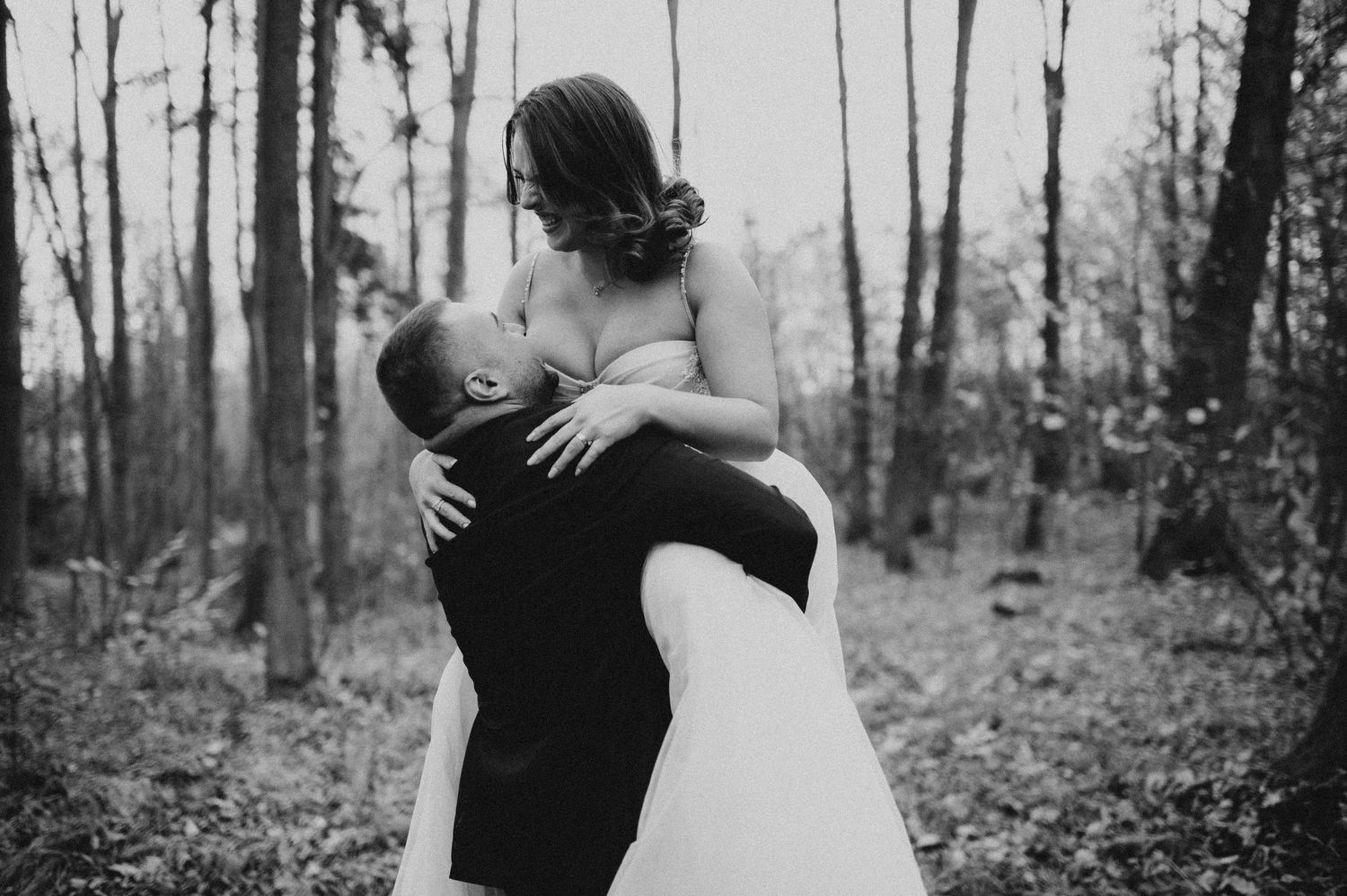 Groom lifting bride in a romantic black and white wedding photo in a forest setting.