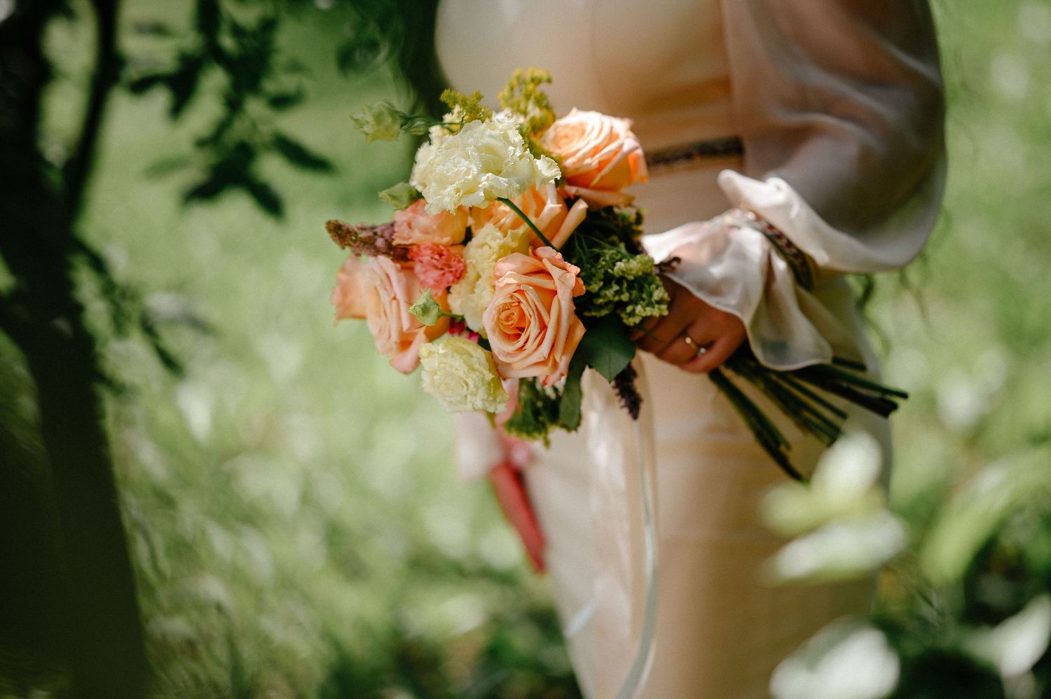 Close-up of a bridal bouquet featuring peach roses, white flowers, and greenery tied with a white ribbon.