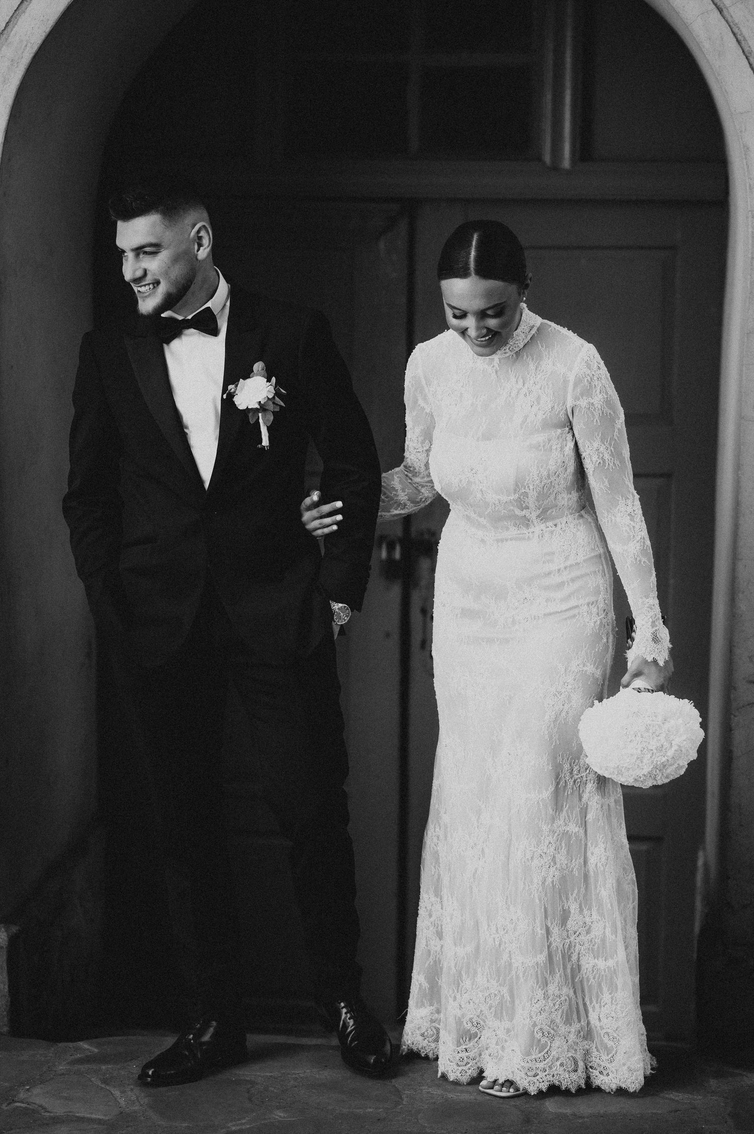Black and white photo of bride and groom smiling as they exit a church doorway on their wedding day.