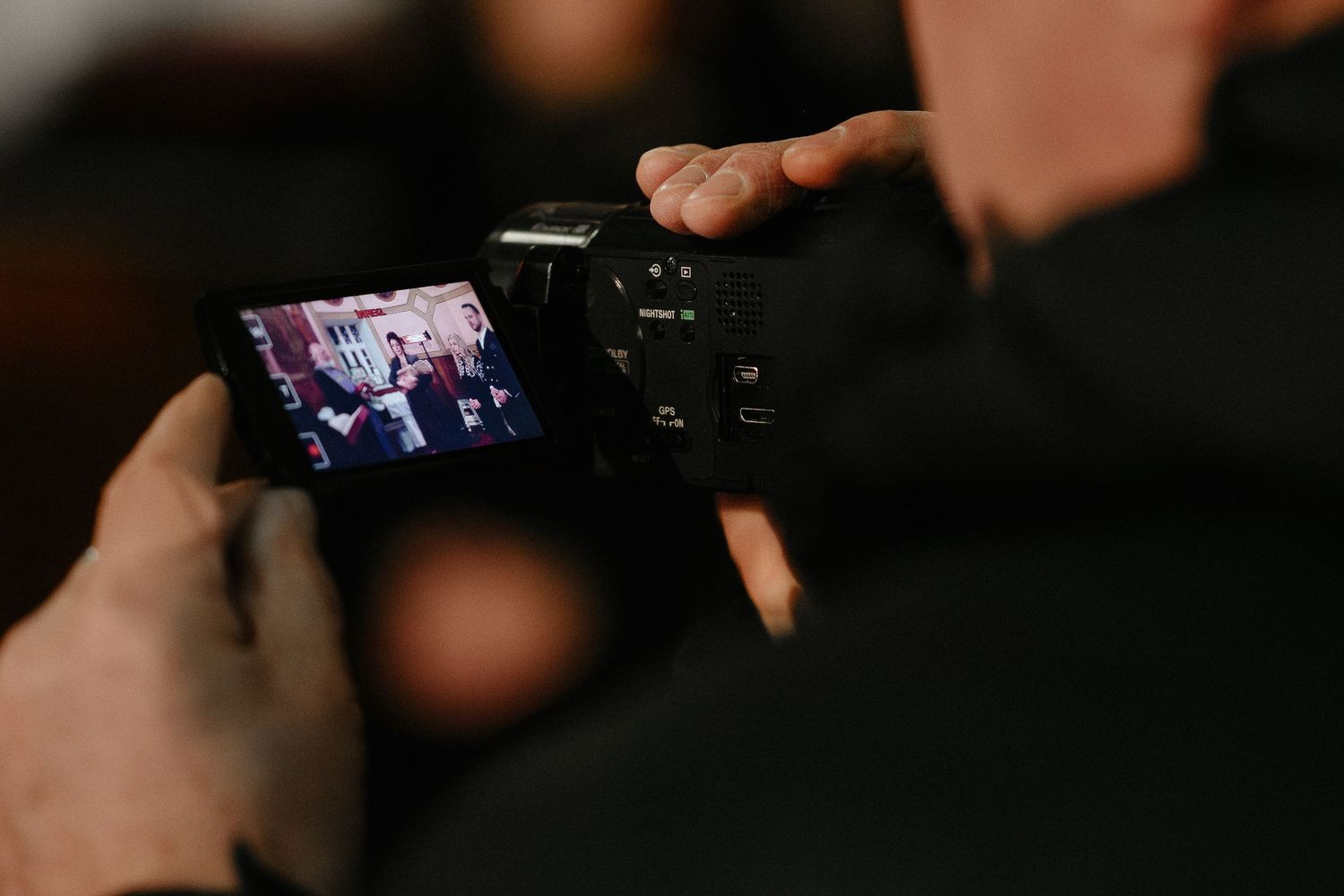 Person holding a digital camera capturing a group photo on the LCD screen.