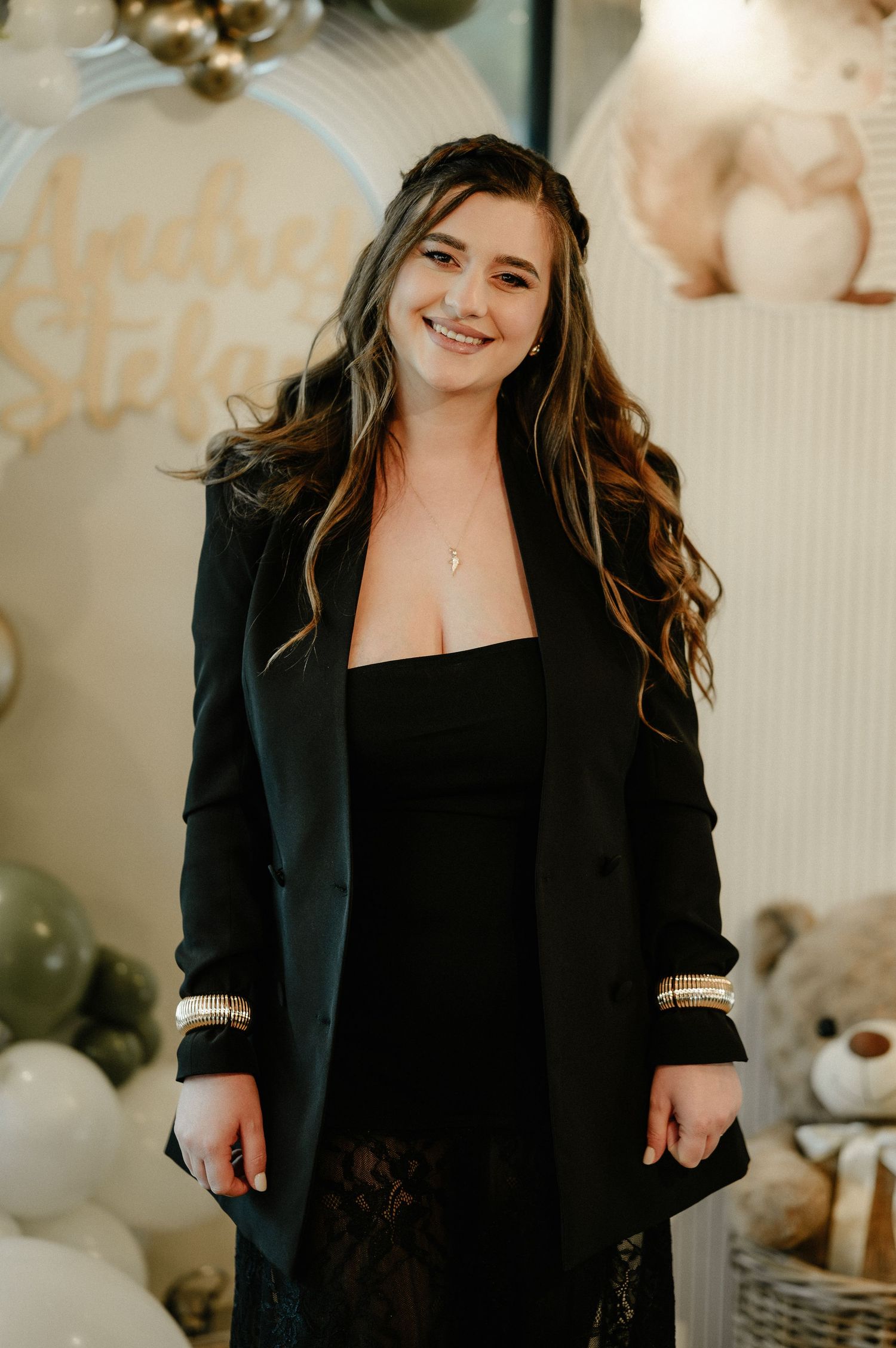 Smiling young woman in black blazer and lace skirt at a festive baby shower celebration.