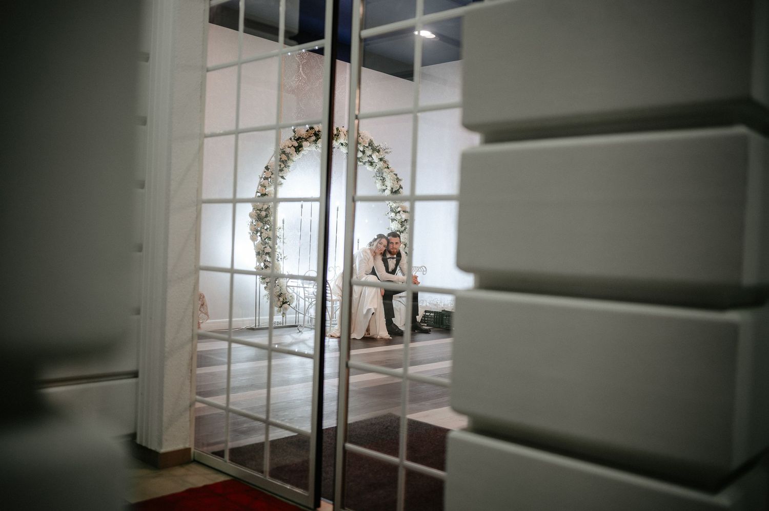 Bride reflected in mirrored wardrobe doors near a circular floral wreath in wedding venue.