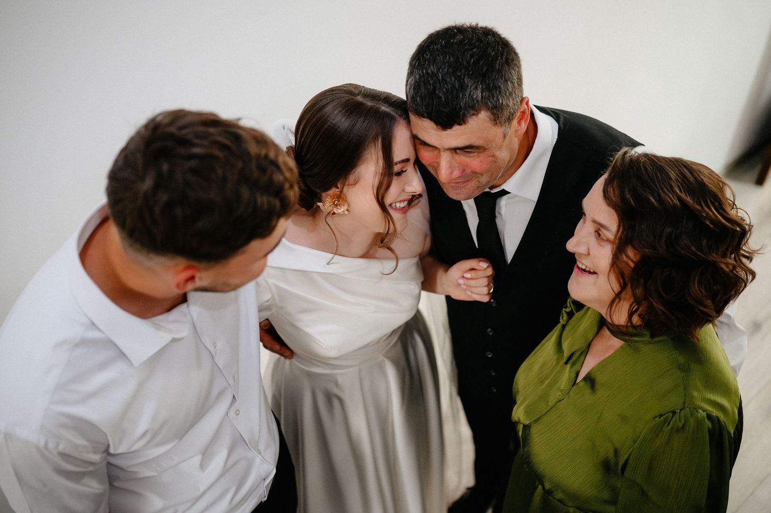 Joyful bride sharing emotional group hug with family members during wedding day celebration.