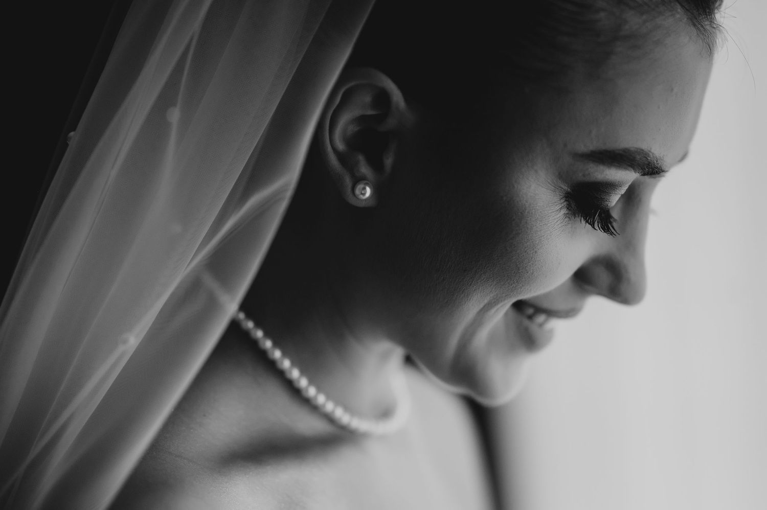 Black and white close-up of a bride wearing pearl earrings and necklace, smiling gracefully.