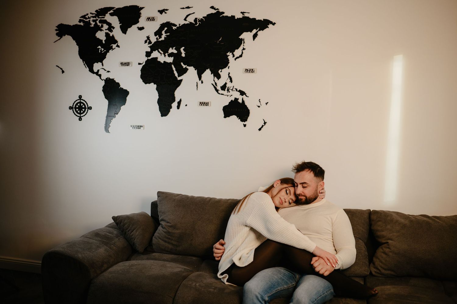Romantic couple cuddling on a gray sofa beneath a large world map wall decoration.