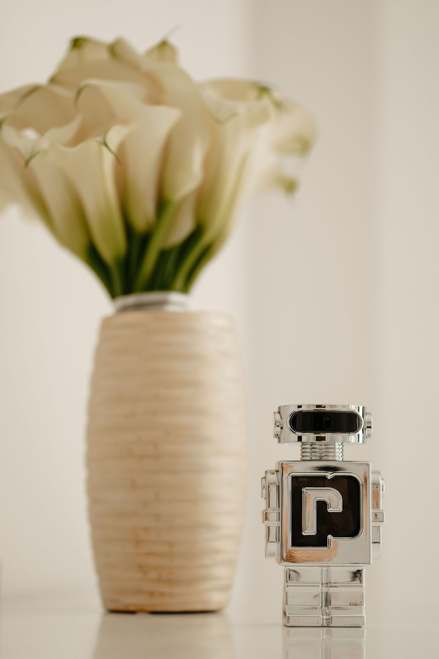 Paco Rabanne Phantom robot-shaped perfume bottle displayed beside white calla lily flower arrangement.